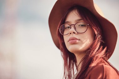 Kendinden emin, uzun saçlı, şapkalı genç kız kameraya bakıyor..