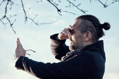 Elinde gözlük olan sakallı, orta yaşlı bir adamın portresi. Kolunu parlak güneşten koruyor..