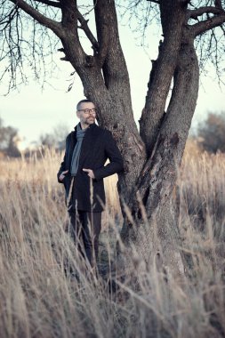 Kırsaldaki bir parkta, bir ağacın yanında ceketli bir adam duruyor. Dinlen, yavaşla, meditasyon yap..