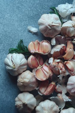 Sarımsaklı karanfil ve koyu dokulu yüzeyde biberiye. Bir dizi sarımsak karanfili ve soğanlı biberiye filizleri koyu, dokulu arka planda serili..