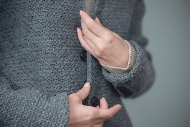 Gri örgü bir ceketin yakın çekimi. Kadın elleri düğmeleri bağlar. Kış, sonbahar sıcak yün giysiler.