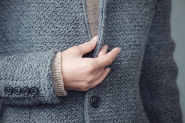 Gri örgü bir ceket ve bir kadının elinin yakın çekimi. Kış, sonbahar sıcak yün giysiler.