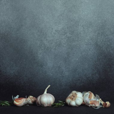 Sarımsak Ampulleri ve karanfiller ve Karanlık Yüzeyde Biberiye. Sarımsak soğanları ve karanfiller taze biberiye filizlerinin yanında koyu bir zemine karşı.