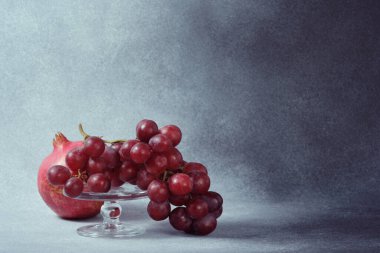 Cam yayaya kırmızı üzümler ve desenli gri yüzeyde nar.