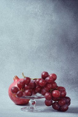 Cam yayaya kırmızı üzümler ve desenli gri yüzeyde nar.