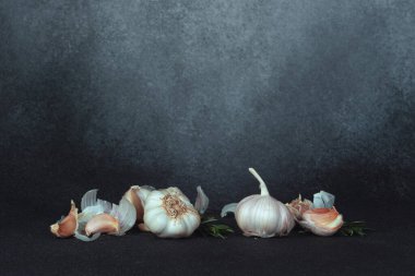 Sarımsak Ampulleri ve karanfiller ve Karanlık Yüzeyde Biberiye. Sarımsak soğanları ve karanfiller taze biberiye filizlerinin yanında koyu bir zemine karşı.