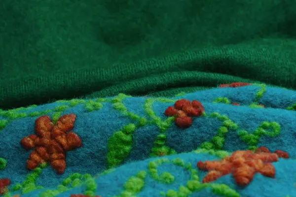 Crafted Felt Fabric. Textured Wool Landscape. Close-up of green and blue wool fabric with red flowers.