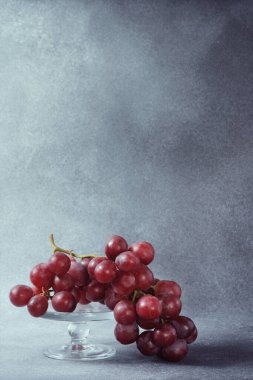 Gri desenli bir arka plana karşı Temiz Cam bir yaylada Taze Kırmızı Üzüm Demeti