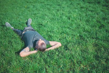Kolları başının arkasında çimenlerde yatan bir adam. Park ortamında açık hava fotoğrafçılığı. Rahatlama ve doğa konsepti. Düz konum.