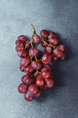 Kaba desenli gri bir yüzey üzerinde kırmızı üzümler demeti