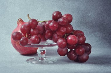 Cam yayaya kırmızı üzümler ve desenli gri yüzeyde nar.