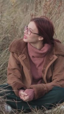 Pembe balıkçı yaka kazaklı ve kahverengi kırbaçlı ceketli gülümseyen genç kız dışarıda neşeli bir konuşma yapıyor. Bulutlu arkaplanı olan bir portre. Sonbahar sezonu ve iletişim konsepti.