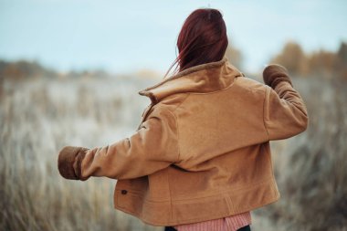 Kolları açık bir kadın, rüzgar saçlarını ve ceketini savuruyor, serin sonbahar melteminin tadını çıkarıyor..