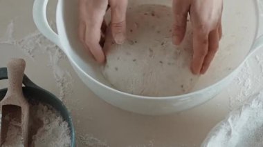 Ellerin ortaya çıktığı ve un kaplı mutfak tezgahında ekmek hamuru şekillendirdiği yakın çekim videosu..