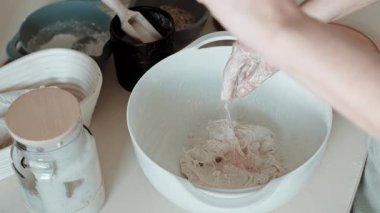 Ellerin mayaya tuz serptiği ve sonra karışımı temiz bir mutfak tezgahında beyaz bir kasede yoğurduğu yakın çekim videosu..