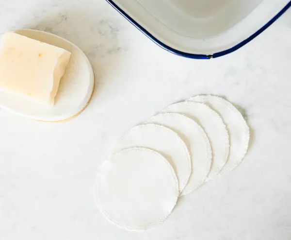 Pamuk göz pedleri art arda sergileniyor. Bir tarafında sabun çubuğu, diğer tarafında kase var.