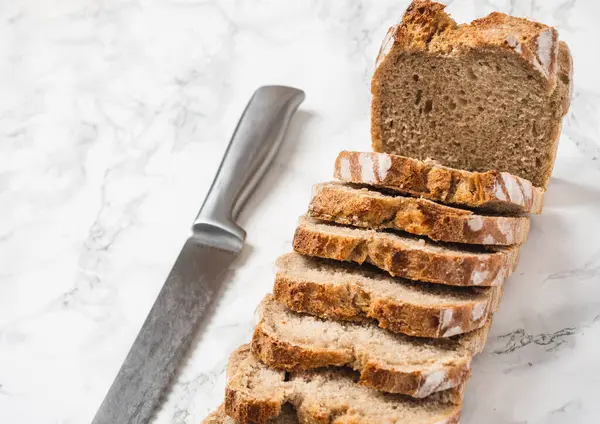 Yanında gümüş bir bıçakla dilimlenmiş kahverengi ekmek. Mermer tezgah. Dilimlerin açı görünümü