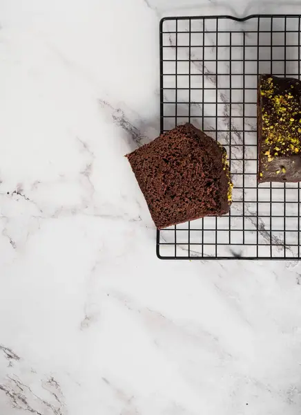 Soğutma rafında dilimlenmiş pasta ve yanında daha büyük bir dilim pasta. Arkaplan olarak beyaz mermer tezgah