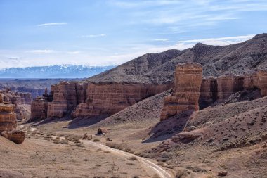 Kazakistan çölündeki dev Charyn Kanyonu. Ufukta dağları ve karlı zirveleri olan çöldeki büyük bir kanyonun panoramik görüntüsü. Gökyüzündeki bulutlar