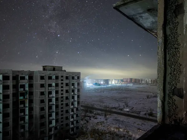 Kış şehri manzarası terk edilmiş evlerle yıldızların arka planına karşı. Yerleşim yerleri uzakta parıldıyor. Kuzey Kutup Dairesi 'nin çok ötesinde.