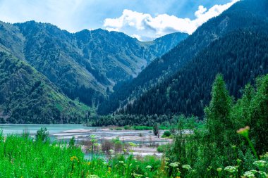 Issyk Gölü, Almaty, Kazakistan. Dağların ve yeşil çimenli ağaçların arka planında mavi suyu olan dağ gölü