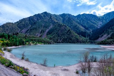 Issyk Gölü, Almaty, Kazakistan. Çok güzel bir manzara. Dağların ve yeşil çimenli ağaçların arka planında mavi suyu olan dağ gölü