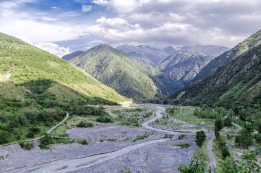 Almaty Ulusal Parkı, Kazakistan. Dağların ve büyük bulutların ardında bir dağ nehri bir geçitten geçiyor.