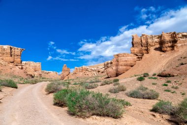 Büyük Charyn Kanyonu, Almaty, Kazakistan. Kaleler Vadisi. Parlak mavi gökyüzü, çöl kanyonunun üzerindeki beyaz bulutlarla sıcak ve güneşli bir günde seyrek bitki örtüsüyle. İnsanlar olmadan