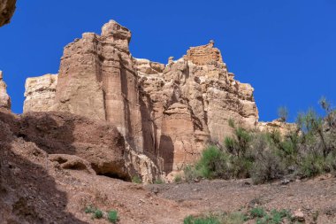 Büyük Charyn Kanyonu, Almaty, Kazakistan. Kaleler Vadisi. Sıcak ve güneşli bir günde, çöldeki büyük bir kayanın üzerinde beyaz bulutlar ve açık mavi gökyüzü. İnsanlar olmadan
