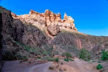 Büyük Charyn Kanyonu, Almaty, Kazakistan. Kaleler Vadisi. Sıcak ve güneşli bir günde, çöldeki büyük bir kayanın üzerinde beyaz bulutlar ve açık mavi gökyüzü. İnsanlar olmadan