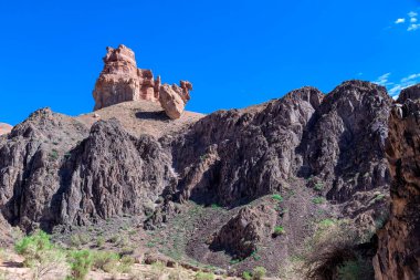 Büyük Charyn Kanyonu, Almaty, Kazakistan. Kaleler Vadisi. Sıcak ve güneşli bir günde, çöldeki büyük bir kayanın üzerinde beyaz bulutlar ve açık mavi gökyüzü. İnsanlar olmadan
