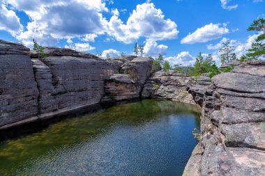 Karkaralinsk, Kazakistan. Göl - Havuz. Ormandaki kayaların arasına sıkıştırılmış su mavi gökyüzüne karşı beyaz kümülüs bulutlarıyla.