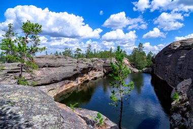 Karkaralinsk, Kazakistan. Göl - Havuz. Ormandaki kayaların arasına sıkıştırılmış su mavi gökyüzüne karşı beyaz kümülüs bulutlarıyla.