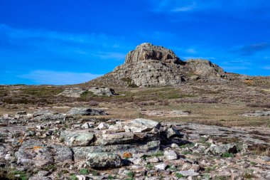 Mavi gökyüzünün altındaki bulutlu kayaların arasında dağılan yalnız, yüksek taştan bir dağ. Tam renkli yatay fotoğraf. Kazakistan, Taldy ve Karaganda 'nın basamakları. Baş dağ