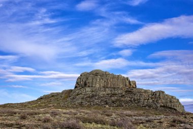 Mavi gökyüzünün altındaki bulutlu kayaların arasında dağılan yalnız, yüksek taştan bir dağ. Tam renkli yatay fotoğraf. Kazakistan, Taldy ve Karaganda 'nın basamakları. Baş dağ