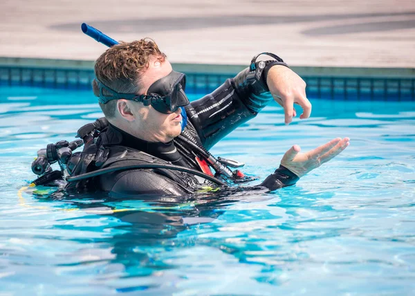 Scuba dive instructor teaching and explaining to students skills in the pool with his hands