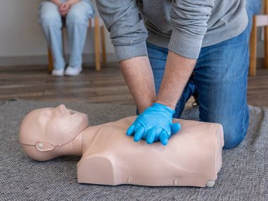Elleri yakın çekim. Erkek öğrenci, ilk yardım eğitimi sırasında bir temel yaşam destek ünitesinde (BLS) göğüs sıkıştırma tekniği uyguluyor..
