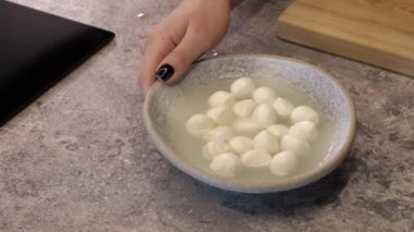 Mozzarella peyniri topları. Bir el masaya bir tabak peynir koyar.