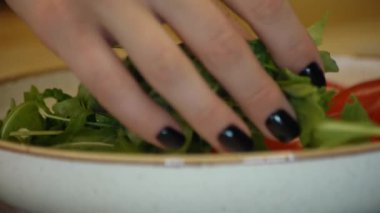 Kız domatesli bir tabağa yeşil roka koyar..