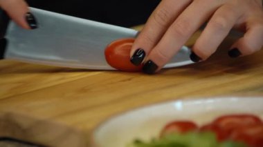 Salata için vişneli domates doğrayan kadın. Dişi eller tahtada kiraz domatesleri kesiyor..