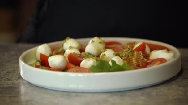 家庭料理の職場で新鮮な野菜を塩漬けにしているヨーロッパの女性カペラサラダ スローモーションで ヨーロッパの女性 野菜サンドイッチに塩を追加 新しいスナックのレシピ モッツァレラボール — ストック動画