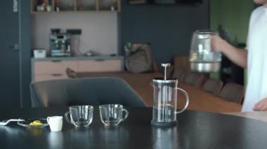 Bir fincan çay yapma genç yetişkin erkek. Kaynar su ısıtıcısı sonlandırır ve onun kupa kaynar su dökülen.