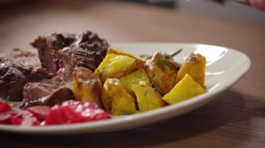 Çatallı bir adam kızarmış patates ve ızgara sebze ve et yiyor.