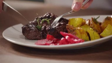 Bir adam bir tabakta et keser ve restoranda ızgara sebzeli kızarmış patates yer.