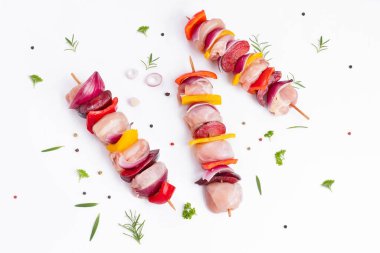 Skewers with pieces of raw meat, red, yellow and green pepper.Top view.Raw chicken leg meat skewers with vegetables,plums,peppers,onions, on a white background.Uncooked mixed meat skewer with peppers.