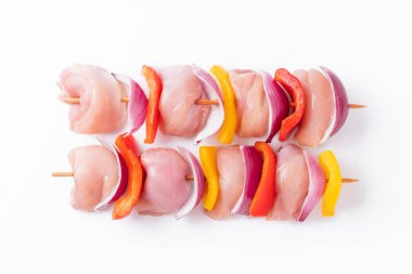Skewers with pieces of raw meat, red, yellow and green pepper.Top view.Uncooked mixed meat skewer with peppers.Raw chicken leg meat skewers with vegetables, peppers, onions, on a white background.