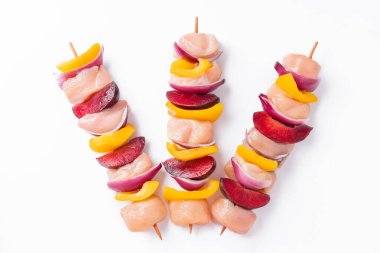 Uncooked mixed meat skewer with peppers.Raw chicken skewers with vegetables, peppers,plums,onions, on a white background.Skewers with pieces of raw meat, red, yellow and green pepper.Top view.