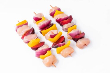 Raw chicken skewers with vegetables, peppers,plums,onions, on a white background.Skewers with pieces of raw meat, red, yellow and green pepper.Top view.Uncooked mixed meat skewer with peppers.