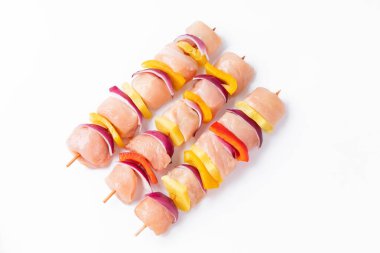 Raw pieces of chicken skewers with pepper onion and pineapple on a white background.Uncooked mixed meat skewer with peppers.Skewers with pieces of raw meat, red, yellow and green pepper.Top view.