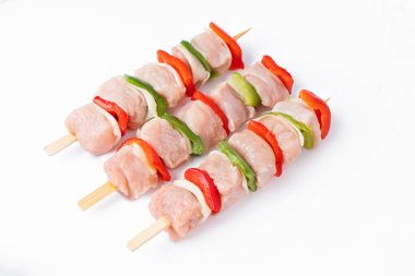 Skewers with pieces of raw meat, red, and green pepper, on white background.Uncooked mixed meat skewer with peppers.Raw turkey skewers with vegetables, peppers, onions on a white background.Top view.